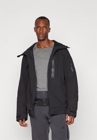 Black insulated jacket with a hood, two zippered chest pockets, elastic cuffs, and a textured finish, worn over a gray shirt.