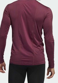 Długi rękaw w bordowej koszulce sportowej o gładkiej teksturze, z dopasowanym krojem, subtelnymi szwami i okrągłym dekoltem z tyłu.