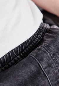 Črne jeans hlače z elastičnim pasom, ki se ponašajo z mehkobo in rahlim izbledeljem. V kombinaciji z oprijeto belo majico v predelu pasu.