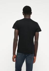 Svart t-skjorte med korte ermer laget av bomull, med rund hals og et enkelt design, båret med blå jeans.