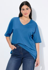 Blue, short-sleeve V-neck t-shirt made of soft fabric, featuring a relaxed fit and side slits, worn with dark denim jeans.