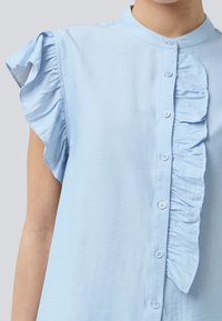Light blue short-sleeve blouse featuring a button-down front, ruffled accents on shoulders, and a smooth fabric texture.