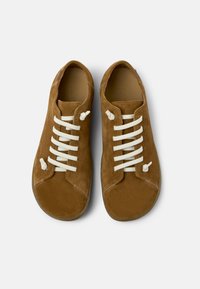 Zapatillas de ante marrón con cordones crema, punteras redondeadas y un mínimo de costuras. Textura suave y diseño limpio.
