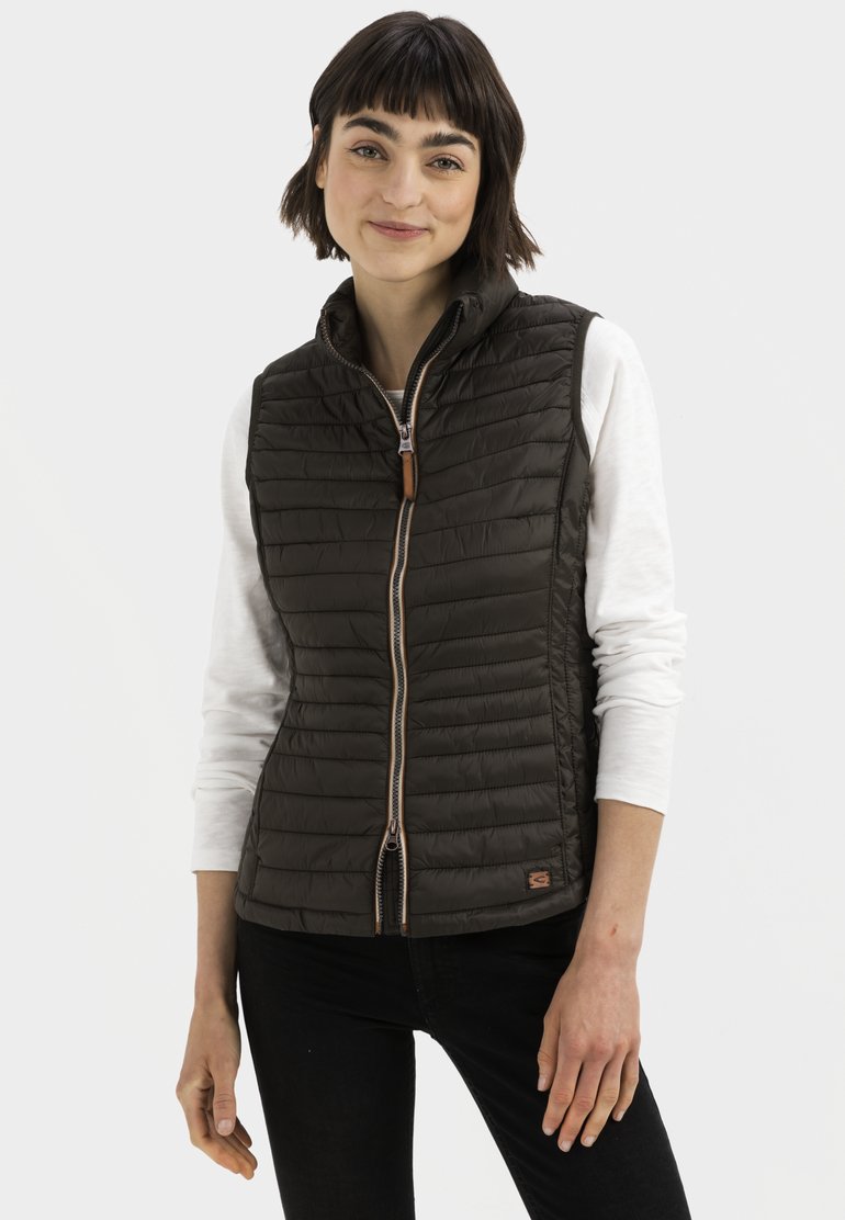Donkergroen zonder mouwen vest met een gewatteerde textuur, rits aan de voorkant en een bruine leren trekband, gedragen over een witte langemouwen shirt.