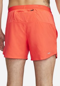 Helle orange Laufshorts aus leichtem Material. Mit einem Mesh-Taillenbund, einer kleinen Reißverschlusstasche und reflektierenden Akzenten.