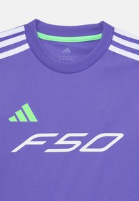 Violets sporta krekls ar zaļu Adidas logo, baltiem "F50" uzrakstiem un baltām plecu svītrām, izmērs 11-12 gadi norādīts kaklā.