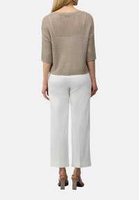 Beige Strickpullover mit lockerer Passform, Dreiviertelärmeln und strukturiertem Muster, kombiniert mit weißen weit geschnittenen Hosen und Sandalen mit Blockabsatz.