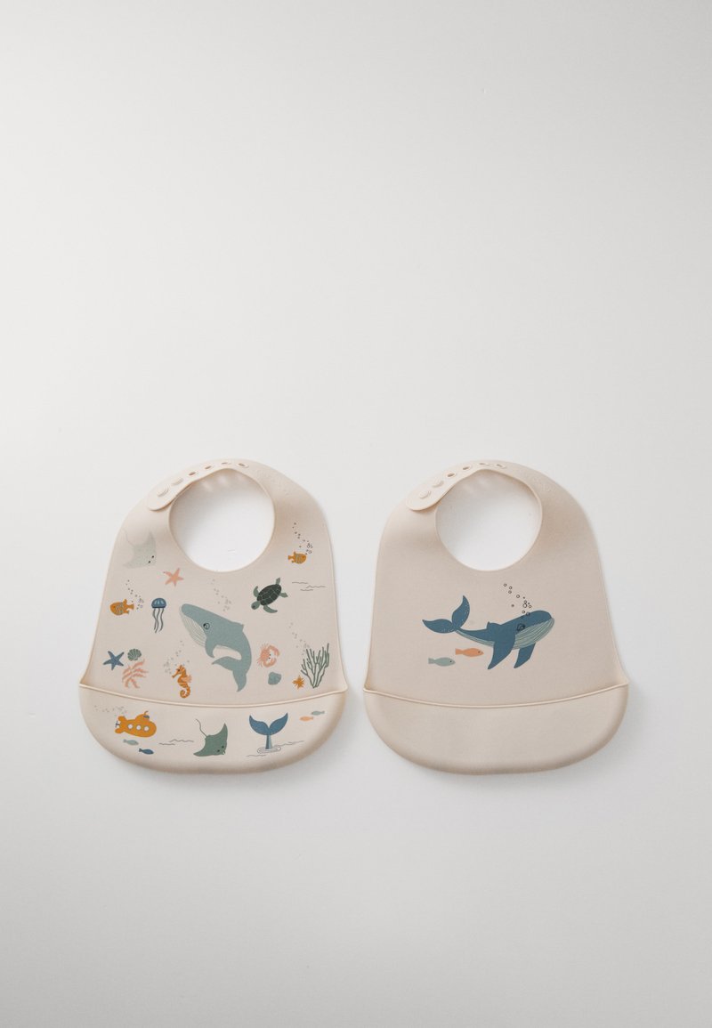 Silicone bibs in soft beige featuring ocean-themed illustrations. Left bib showcases colorful sea life; right bib displays a blue whale design.