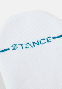 Witte sok met turquoise "STANCE" logo en horizontale accentstrepen. Heeft een ribbeltextuur en een gladde stofafwerking.