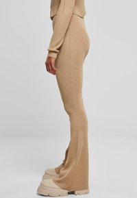 Pantalons évasés en tricot côtelé beige, ajustés à la taille. Tissu texturé avec des lignes verticales, accompagnés de chaussures à plateforme chunky beige.