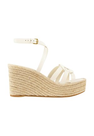 Sandale compensée blanche avec semelle plateforme en jute tressée et bride de cheville avec boucle dorée sur fond blanc.