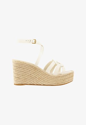 Sandale compensée blanche avec semelle plateforme en jute tressée et bride de cheville avec boucle dorée sur fond blanc.