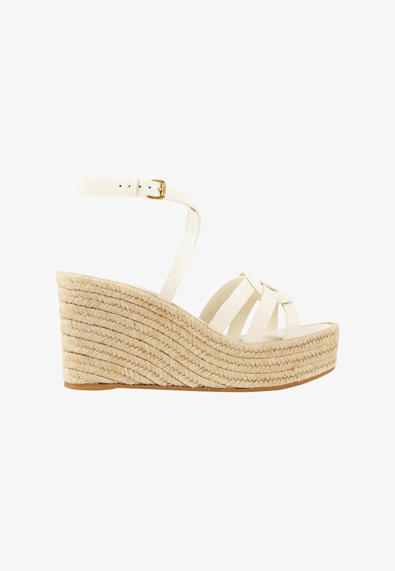 Sandale compensée blanche avec semelle plateforme en jute tressée et bride de cheville avec boucle dorée sur fond blanc.
