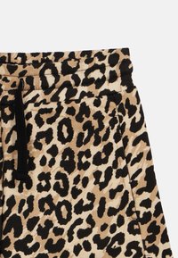 Tissu à imprimé léopard avec cordon de serrage noir et taille élastique, montrant une partie d'un vêtement avec couture latérale et détail de poche.