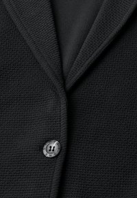 Blazer noir texturé avec un col cranté et un seul bouton noir étiqueté "ONE STREET."