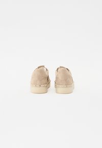 Chaussures en nubuck beige avec une forme arrondie, ornées d'accents de clous dorés le long de la semelle et d'une petite languette à l'arrière.