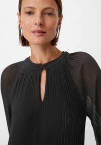 Schwarze, plissierte Bluse mit hohem Ausschnitt und Schlüssellochdetail; lange, durchscheinende Ärmel; glatte Textur und dezenter Glanz.