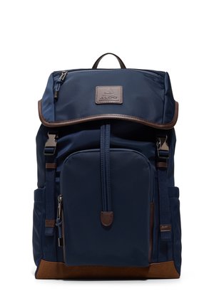 Mochila azul marino con bolsillo frontal con cremallera, borde inferior marrón, solapa superior con cierre, bolsillos laterales y parche con el logo de Aldo en la solapa.