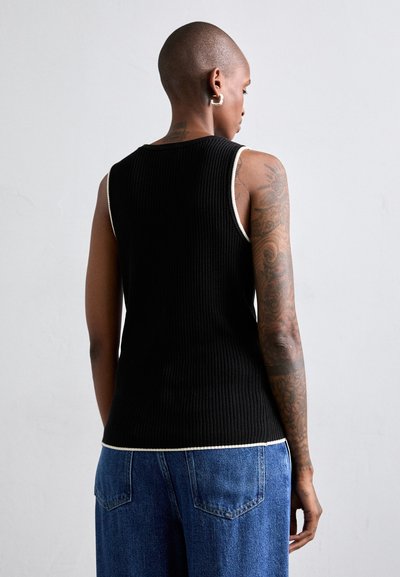 Czarny ribbed tank top z kontrastowym białym wykończeniem na dekolcie i brzegu, prezentujący dopasowany krój. Noszony z niebieskimi spodniami typu wide-leg.