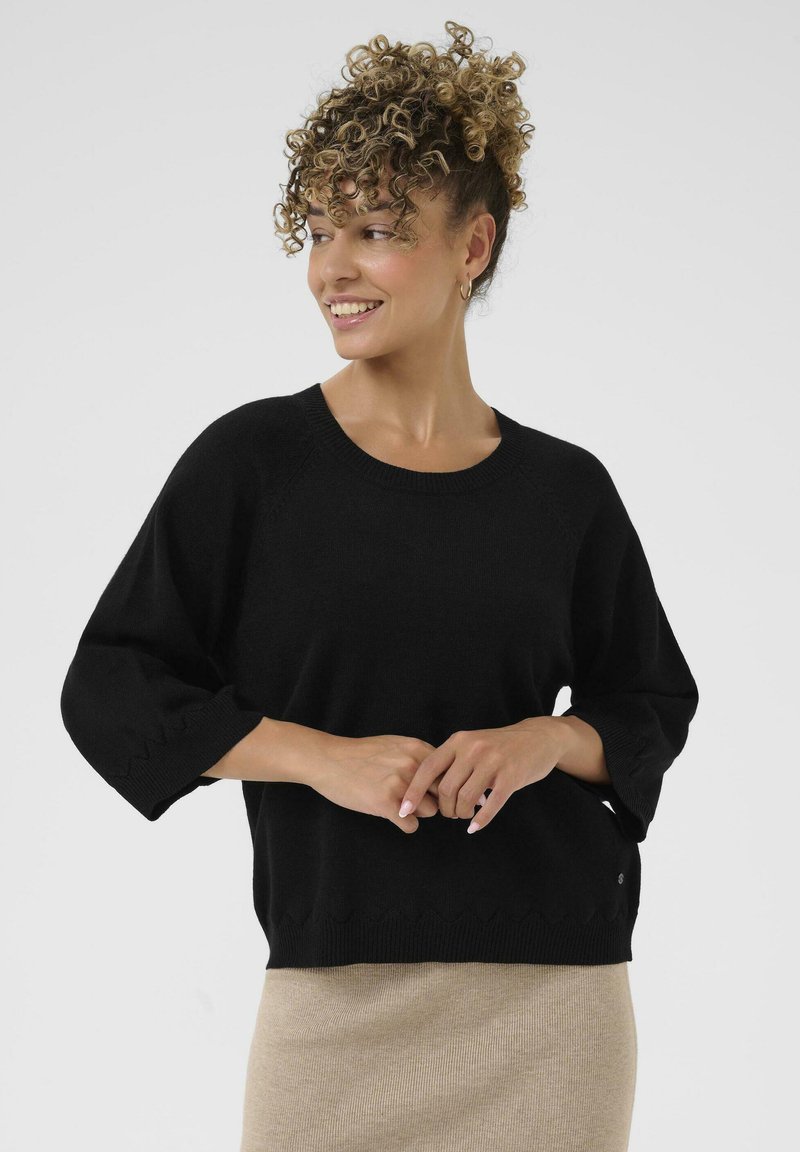 Črn pleten pulover z okroglo odprtino in dolžino rokavov do tretjine. Ima detajle z valovitimi robovi in mehak videz.