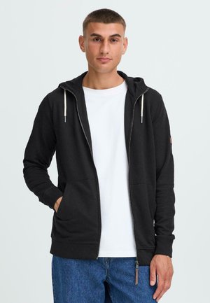 Black zip-up hoodie with drawstrings, two front pockets, and ribbed cuffs. Paired with a white T-shirt and blue jeans. Smooth texture.