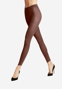 Leggings marron en matière lisse et extensible. Ils ont une taille haute et une silhouette ajustée, associés à des chaussures à talons hauts noires.