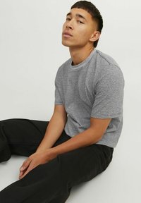 Šedý a bílý pruhovaný krátký rukáv T-shirt s kulatým výstřihem, spárovaný s černými širokými kalhotami, sedící na neutrálním pozadí.