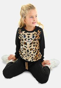 Schwarzes Sweatshirt mit einem plüschigen Leoparden-Gesichtsdesign; warme Textur; schwarze Hose; weiße Sneaker; mit verspielten Details wie großen Augen und Ohren.