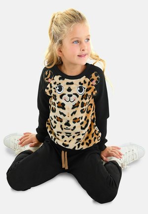 Felpa nera con design di un volto di leopardo in peluche; texture calda; pantaloni neri; sneakers bianche; presenta dettagli giocosi come occhi e orecchie grandi.