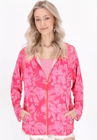 Giacca rosa floreale con zip, realizzata in un tessuto leggero, dotata di cappuccio, tasche e una zip arancione a contrasto. Texture liscia con un motivo tropicale.