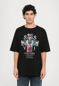 Black oversized t-shirt featuring a vibrant graphic design with a butterfly, rose, and text "88 VJ COUTURE LIMITED EDITION FALL/WINTER 25-26."