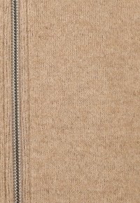 Beige knit fabric with a smooth texture, featuring a silver zipper running vertically along one side. No visible patterns or accents.