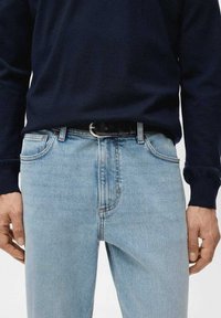 Vaqueros de mezclilla azul claro con un corte clásico, que cuentan con cinco bolsillos y un cinturón oscuro con hebilla plateada. Combinados con un suéter azul marino.