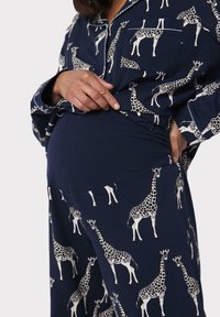 Navy pyjama-set met witte giraffenpatronen, gemaakt van zachte stof. Het shirt heeft een zak aan de voorkant; elastische tailleband voor comfort.