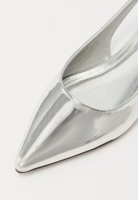 Sudraba metāla izgulētie apavi ar apsīpolētām purngaliem, glitu un spīdīgu apdari, izgriezumiem sānos un gludu iekšējo oderi, ar melnu zoli.