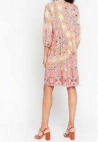 Blommönstrad klänning i kräm, rosa och blått med trekvartsärmar och insvängd midja. Har en lagd nederkant och en avslappnad passform.