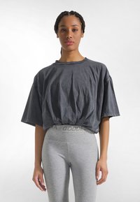 Donkergrijs oversized T-shirt met korte mouwen, getailleerd bij de taille. Gecombineerd met lichtgrijze legging met een logo op de tailleband.