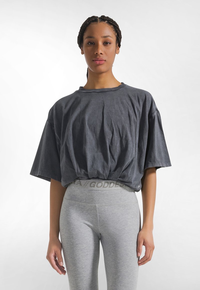 Donkergrijs oversized T-shirt met korte mouwen, getailleerd bij de taille. Gecombineerd met lichtgrijze legging met een logo op de tailleband.