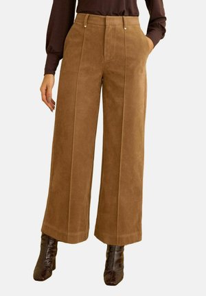 Bukser i kamelbrun med vide ben, forreste presseriller og sidelommer, båret sammen med mørkebrune ankelstøvler med hæl og en matchende langærmet top.