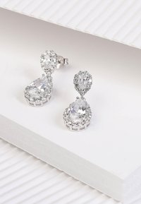 Ohrringe in Silberoptik mit teardrop-förmigen klaren Edelsteinen, umgeben von kleineren Kristallakzenten, die in einem filigranen Design angeordnet sind.