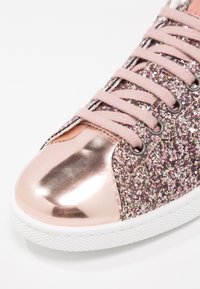 Sneaker rosa scintillante con punta metallica color rosè, tomaia in glitter testurizzato e lacci rosa. Dotata di suola in gomma bianca.