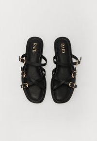Sandales plates noires avec trois fines sangles entrecroisées, des boucles dorées, un bout carré arrondi et un matériau en cuir synthétique texturé.