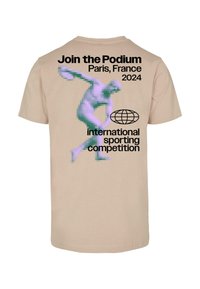 Beige tričko s pixelovanou fialovou postavou v pohybu, černý text s nápisem „Připojte se k Podium, Paříž, Francie 2024, mezinárodní sportovní soutěž.“
