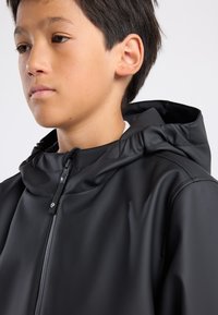 Black waterproof jacket with a front zipper, high collar, and adjustable hood. Smooth texture; seams and logo detail on the zipper pull.