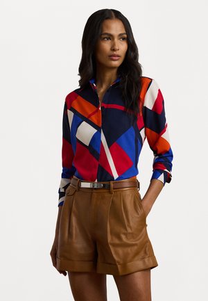 Flerfärgad skjorta med knappar och geometriska mönster i röd, blå, vit och orange; kombinerat med bruna lädershorts och ett silverfärgat bälte.