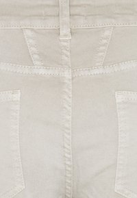 Pantalon en denim beige avec une coupe ajustée, des poches arrière et des détails de couture horizontale le long de la taille et des coutures.