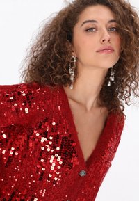Rode pailletten cardigan met een V-hals ontwerp, textuur gebreide stof en een zilveren knoopdetail. Heeft een getailleerde pasvorm en glinsterende accenten.