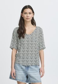 T-shirt à manches courtes en motif géométrique noir et blanc. Design en V, coupe décontractée, associé à un short en denim clair.