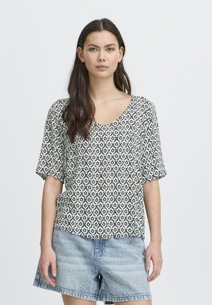 Short-sleeve top in white and black geometric pattern. V-neck design, relaxed fit, paired with light denim shorts.