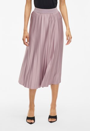 Jupe midi plissée en tissu lavande doux, dotée d'une large ceinture élastique et d'une silhouette fluide. Portée avec des talons ouverts noirs.